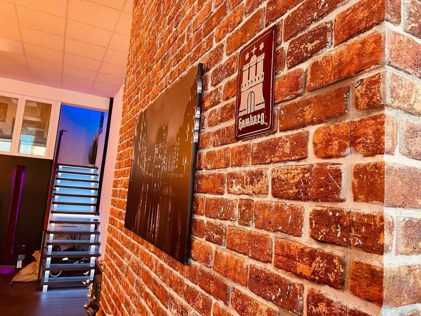 Backsteinwand im Eingangsbereich mit Hamburg-Schild und Treppe, stimmungsvolle Beleuchtung in der Physiotherapiepraxis onebalance Rheinstetten