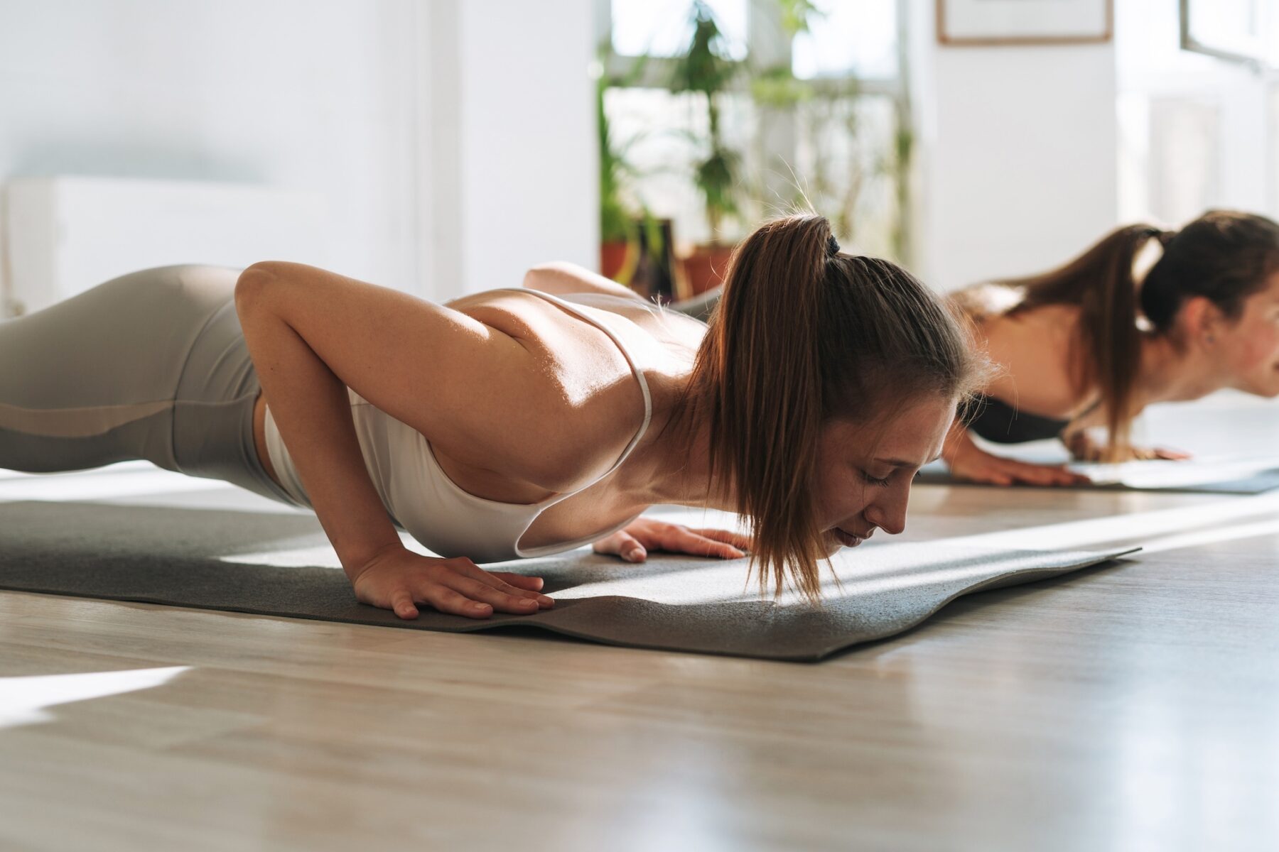 Zwei Frauen trainieren im Wohnzimmer und machen Liegestütze auf Yogamatten bei Tageslicht.